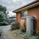 Outdoor hot water system installed beside a Canberra home with light frost on surrounding ground and pipes.