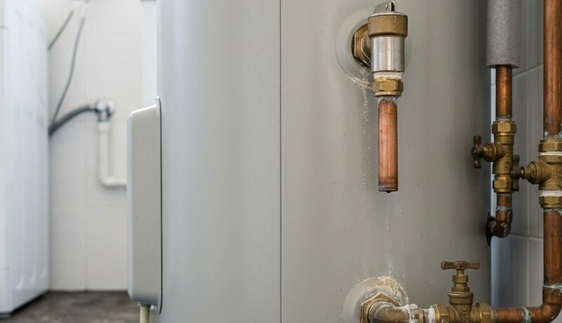 Close-up of a residential hot water system with visible pipework and minor signs of wear in a utility room.